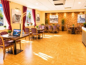 A hotel lobby with wooden flooring, red curtains, and multiple dining tables with chairs. - Hotel Pale Wolfsburg 24H Self Check-in (Wolfsburg)