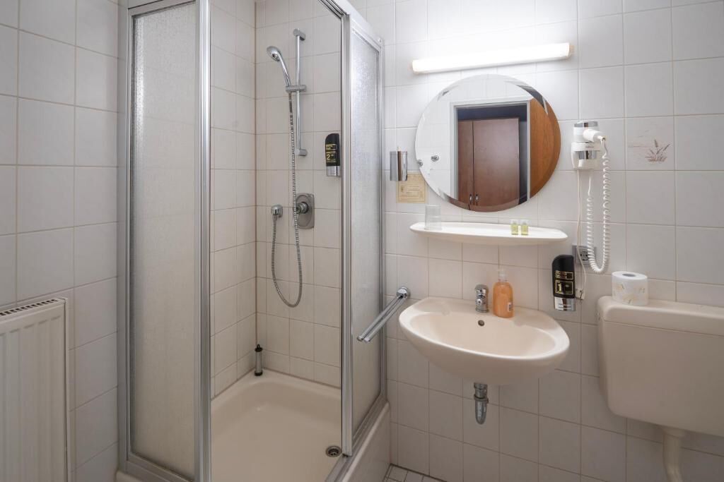 A bathroom with a glass-enclosed shower, a sink, a mirror, and a toilet.