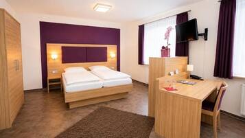 A hotel room with a bed, a desk, a TV, and a window with curtains.