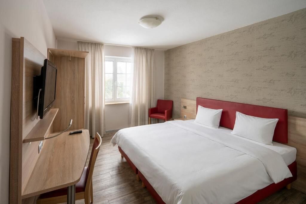 A hotel room with a bed, a desk, a chair, a TV, and a window.