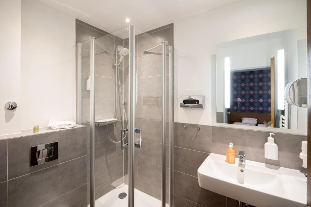 Une salle de bain moderne avec une douche à parois de verre, un lavabo blanc et un miroir.