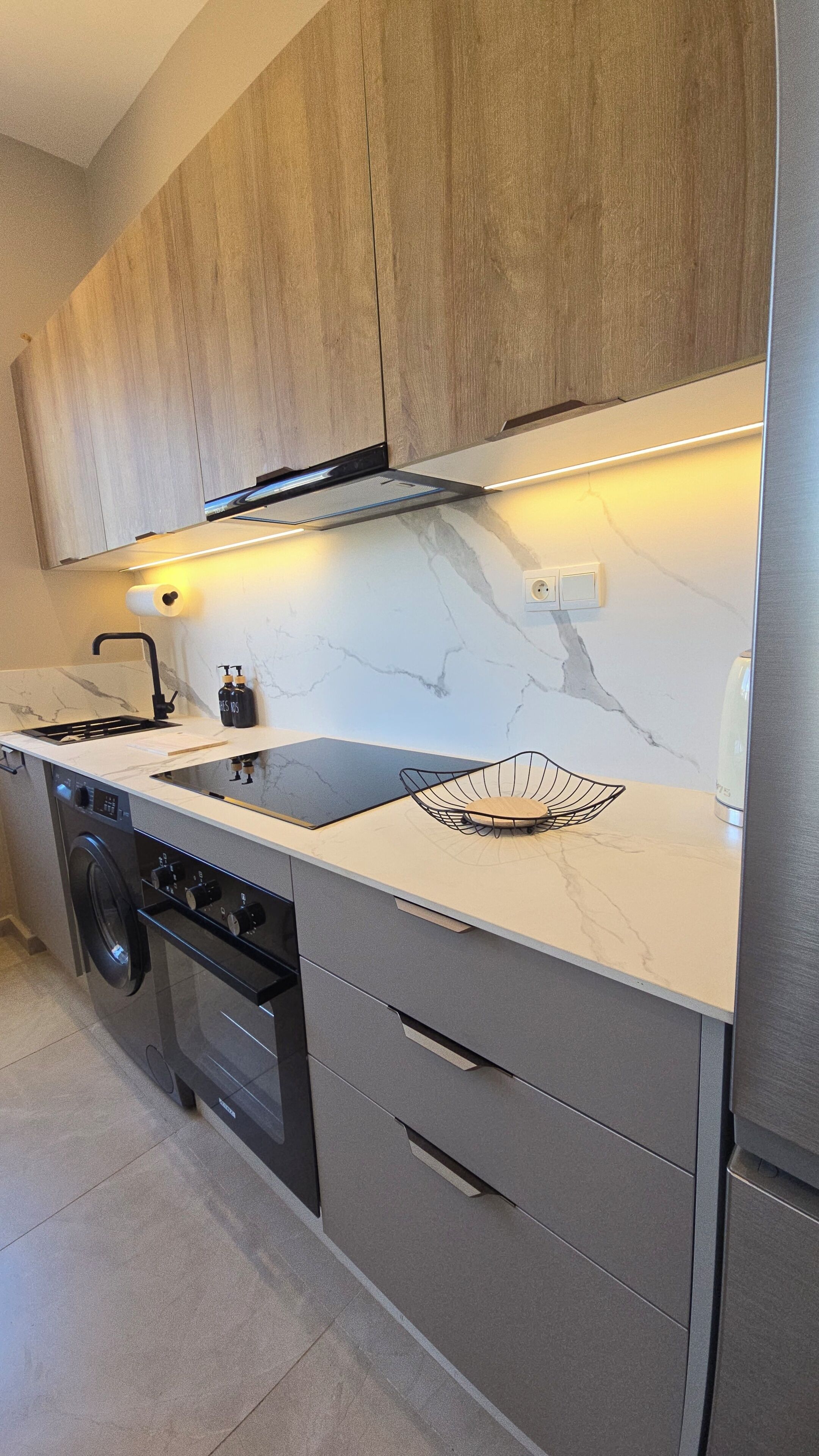 A modern kitchen with wooden cabinets, a built-in oven, a stainless steel sink, and a marble backsplash.