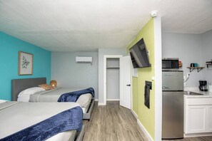 A hotel room with two beds, a kitchenette, a TV mounted on the wall, and a door leading to a bathroom.