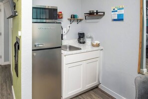 Eine kompakte Küchenzeile mit Kühlschrank, Mikrowelle, Kaffeemaschine und kleinem Spülbecken.