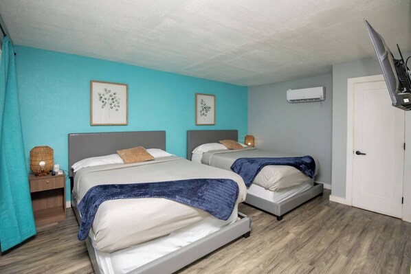 A room with two beds, a TV, and an air conditioning unit.