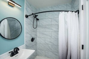 A bathroom with a white sink, a round mirror, a shower with a black curtain, and a towel rack.