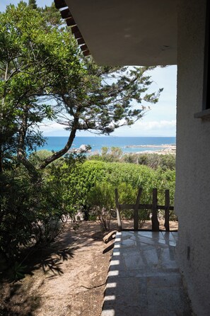 Ein Steinweg führt zu einer überdachten Außenbereich mit Blick auf das Meer und die umliegende Vegetation.