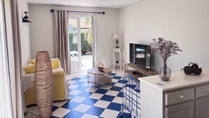 A room with a checkered floor, a sofa, a TV, a lamp, and a vase with dried flowers. - House of the Palm Tree (La Brée-les-Bains)