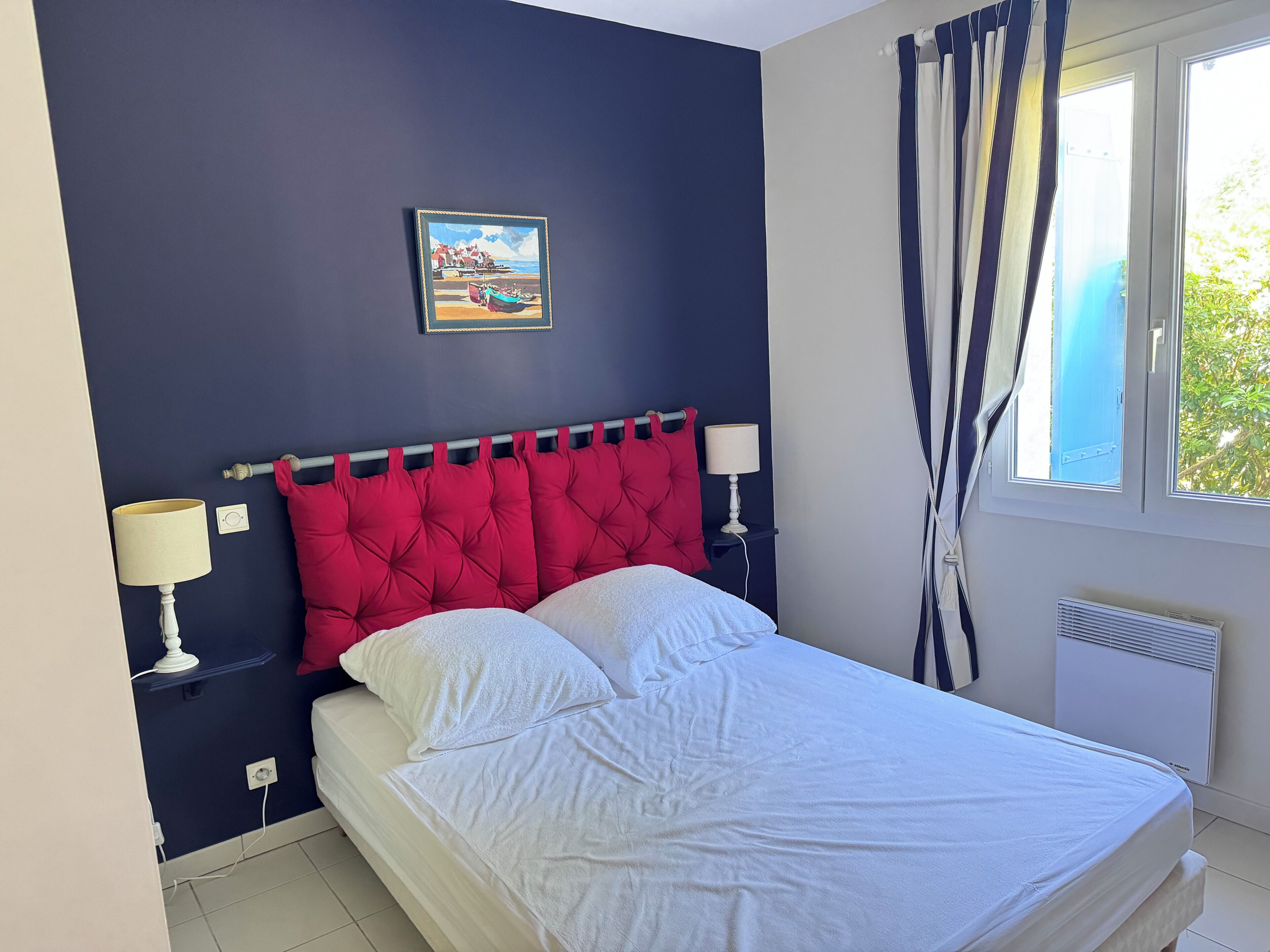 A neatly made bed with white bedding, a red tufted headboard, and two bedside lamps.