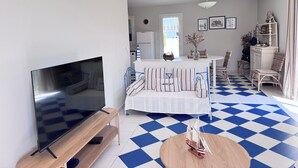 A living room with a TV, a dining area with a table and chairs, a patterned floor, and a small ship model on a table. - House of the Palm Tree (La Brée-les-Bains)