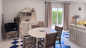 A dining area with wicker chairs, a round table, a white cabinet, and a view through a glass door. - House of the Palm Tree (La Brée-les-Bains)
