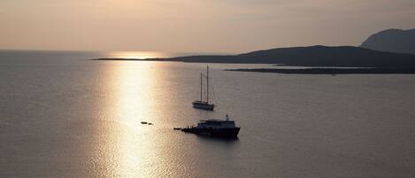 A calm sea with two boats, one larger and one smaller, and a distant landmass under a clear sky.