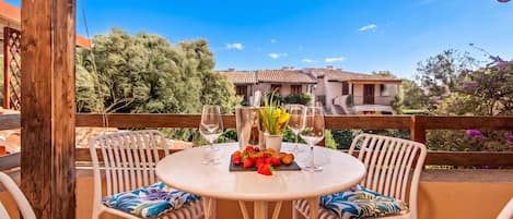 Une terrasse extérieure avec une table ronde, deux chaises, une bouteille de vin et un saladier de fruits.