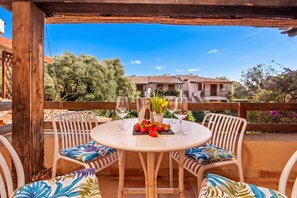 An outdoor patio with a round table, two chairs, a bottle of wine, and a bowl of fruit. - Nido Di Tom (Olbia)