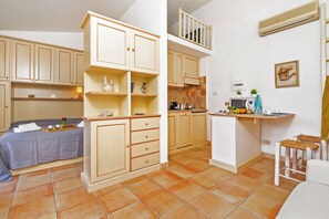 Uma cozinha compacta com armários embutidos, uma área de refeições com mesa e cadeiras, e um pequeno espaço de estar com um sofá.