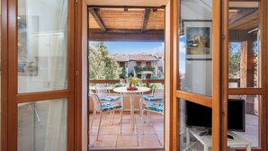 A wooden-framed glass door leading to a patio with a round table, chairs, and a television. - Nido Di Tom (Olbia)