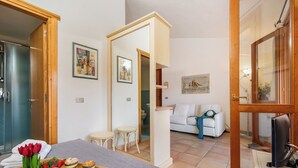 A room with a bed, a TV, a small table with a tray of food, and a white sofa. - Nido Di Tom (Olbia)