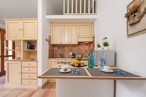 A kitchen with light wooden cabinets, a countertop with a water bottle, a coffee maker, and a fruit bowl. - Nido Di Tom (Olbia)
