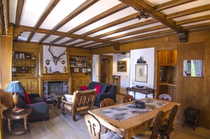 Ein rustikales Interieur mit freiliegenden Holzbalken, Kamin, Bücherregalen und einem Essbereich.