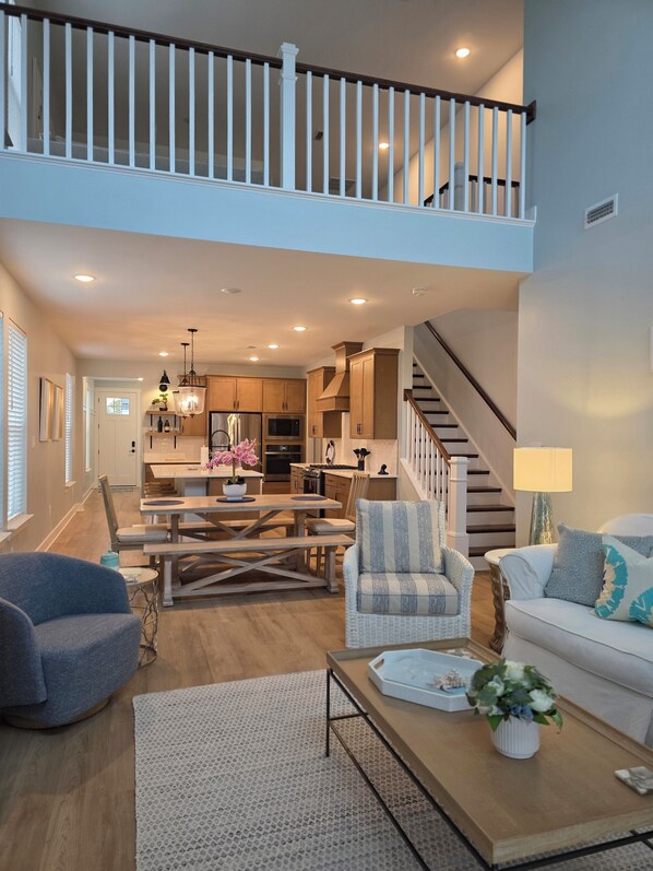 A spacious living area with a dining table, two chairs, a sofa, a coffee table, and a staircase leading to an upper level.