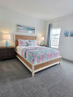 Een netjes opgemaakt bed met een bloemenprint deken, twee bedlampen, een nachtkastje met lade, een hoofdbord en een raam met uitzicht.