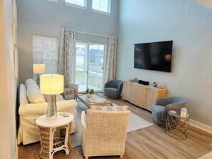 A living room with a sofa, armchair, coffee table, and a TV mounted on the wall.