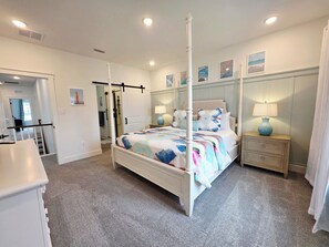A four-poster bed with a floral bedspread, a nightstand with a lamp, and a door leading to a bathroom. - Brand New Spacious 4-bedroom townhome with pool and gym. (Selbyville)