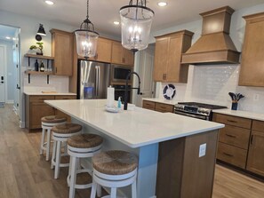 A modern kitchen with wooden cabinets, a central island with stools, stainless steel appliances, and pendant lighting.