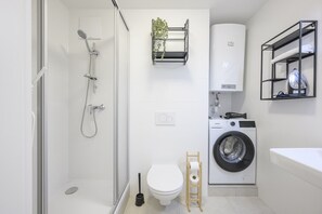 Un bagno moderno con doccia vetro, lavatrice, WC e lavandino.