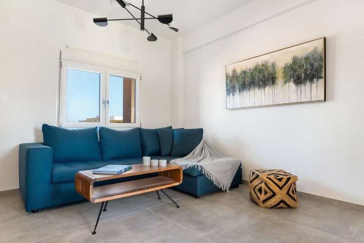 Een moderne woonkamer met een blauwe bank, een houten salontafel en een schilderij aan de muur.