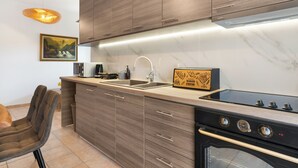 A modern kitchen with wooden cabinets, a built-in stove, a sink, and a pendant light. - Ocean Alley Seaside Retreats (K. Gouves)