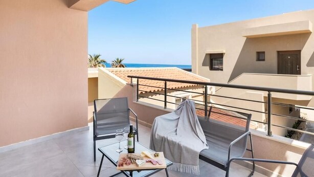 A balcony with a table set for dining, a chair with a blanket, and a view of the sea. - Ocean Alley Seaside Retreats (K. Gouves)