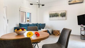 A modern living room with a round dining table, a sofa, and a TV. - Ocean Alley Seaside Retreats (K. Gouves)