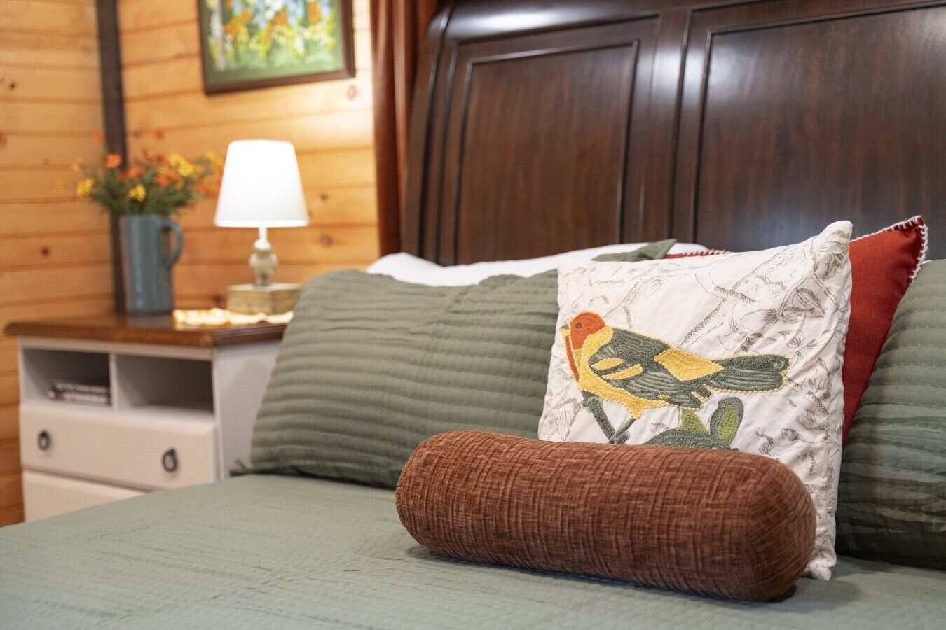 Un letto con una coperta verde, un cuscino marrone e un cuscino decorativo con un motivo a uccello.
