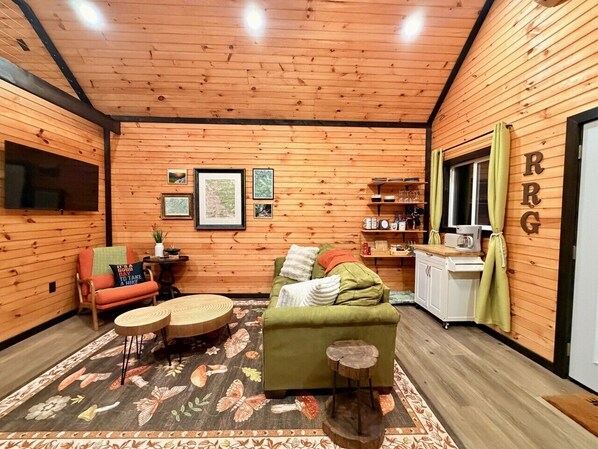 Una habitación acogedora con paredes de madera, un sofá verde, una mesita de centro redonda y una pequeña mesita auxiliar.