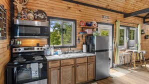 A modern kitchen with wooden cabinetry, stainless steel appliances, and a view of the outdoors. - The Grey Squirrel Hideaway - Hot Tub , Fire-Pit, Pet-Friendly (Campton)