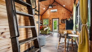 A wooden interior with a loft bed, a dining table with a unique wooden base, and a green sofa. - The Grey Squirrel Hideaway - Hot Tub , Fire-Pit, Pet-Friendly (Campton)