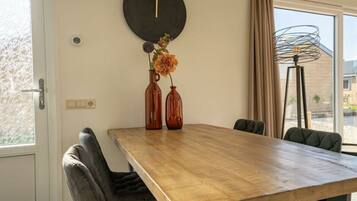 A dining area with a wooden table, two chairs, a wall clock, and a vase with flowers.