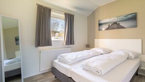 Ein Schlafzimmer mit einem Bett, einem Fenster mit Vorhängen, einem Heizkörper, einem Spiegel und einem Bild an der Wand.