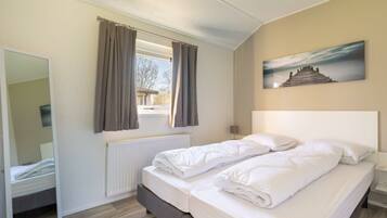 A bedroom with a bed, a window with curtains, a radiator, a mirror, and a painting on the wall.