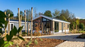 A modern mobile home with a large glass window, surrounded by a gravel driveway and a small garden area.