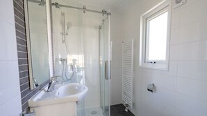 Ein Badezimmer mit Duschkabine, Waschbecken, Toilette und Fenster.