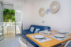 A dining area with a table set for four, a blue sofa, and a balcony with white chairs. - A comfortable 49-square-meter apartment, perfect for five people, located on the third floor (Scala A) of a building with an elevator (NOT suitable for people with disabilities) directly facing the seafront.The property is located in Lignano Sabbiadoro i (Lignano Sabbiadoro)