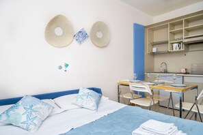 Ein Zimmer mit Bett, Schreibtisch, Stühlen, einem Waschbecken und einer Küchenzeile.