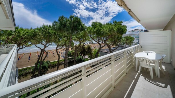 Un balcon avec vue sur la plage, des meubles d’extérieur blancs et une rambarde.