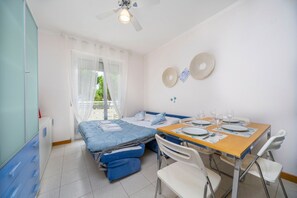 A compact room with a bed, a small dining table with chairs, a ceiling fan, and a window with curtains. - A comfortable 49-square-meter apartment, perfect for five people, located on the third floor (Scala A) of a building with an elevator (NOT suitable for people with disabilities) directly facing the seafront.The property is located in Lignano Sabbiadoro i (Lignano Sabbiadoro)