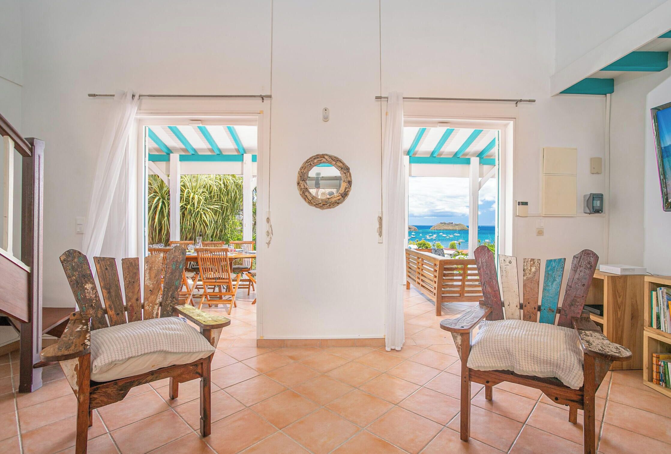 A spacious room with a view of the sea, featuring two wooden chairs, a dining table, and a bookshelf.
