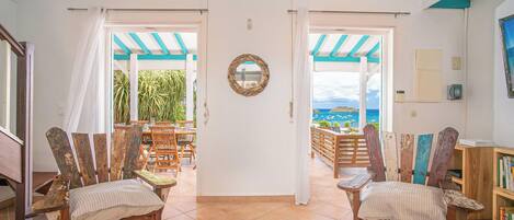 A spacious room with a view of the sea, featuring two wooden chairs, a dining table, and a bookshelf.