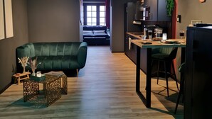 A modern living space with a sofa, dining table, kitchen area, and a view into the bedroom.