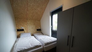 Ett litet, kompakt rum med två enkelsängar, ett fönster med persienner och en garderob.